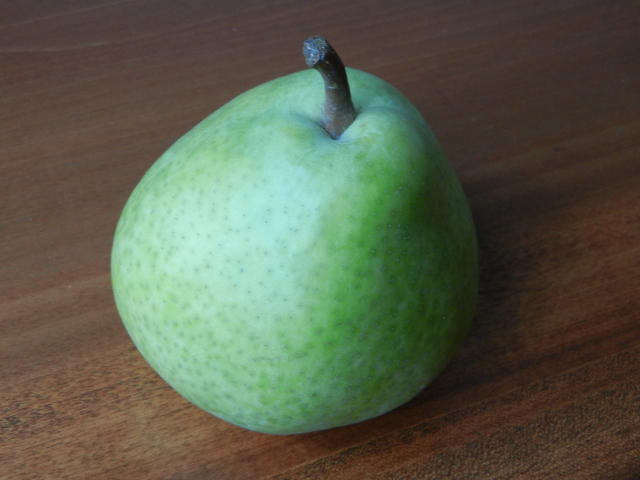 A green pear with an almost bluish tinge, on a wooden surface