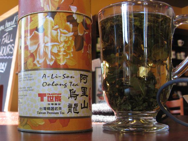 A canister of oolong tea, tradition brand, and a glass mug with loose-leaf tea brewing in it