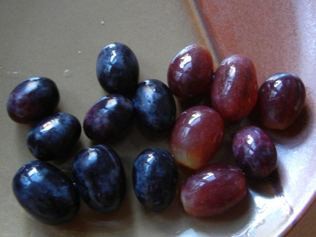 Whole black grapes on the left, whole red grapes on the right, on a brown ceramic plate