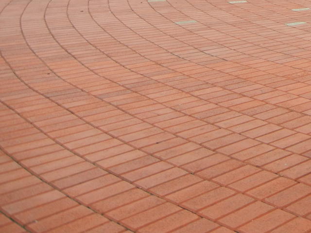 Red sidewalk bricks laid out in a circular pattern, radiating from a spot off the photo to the upper right