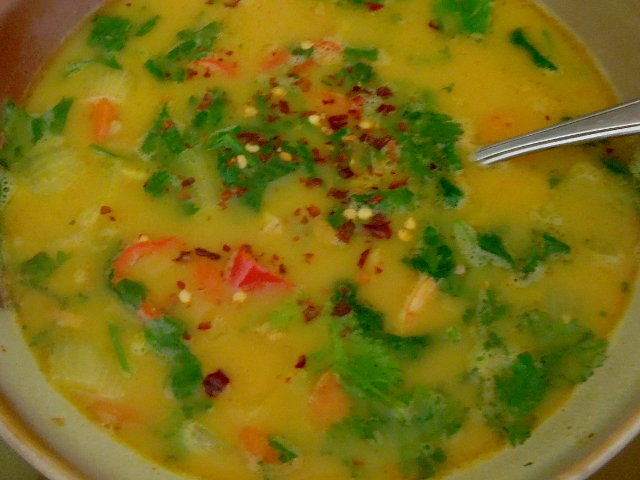 A bowl of coconut curry soup, with a rich yellow broth and bright green cilantro leaves