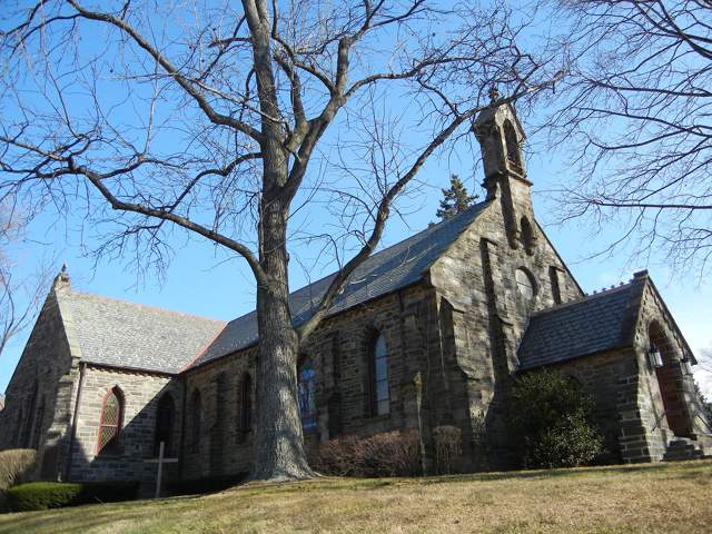 A stone church in winter, with a large leafless tree, taken from a low angle.