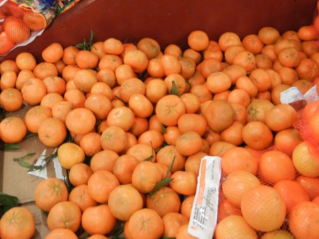 Whole, fresh Mandarin oranges, a small, flat, orange-shaped citrus fruit, with a few stems and leaves attached
