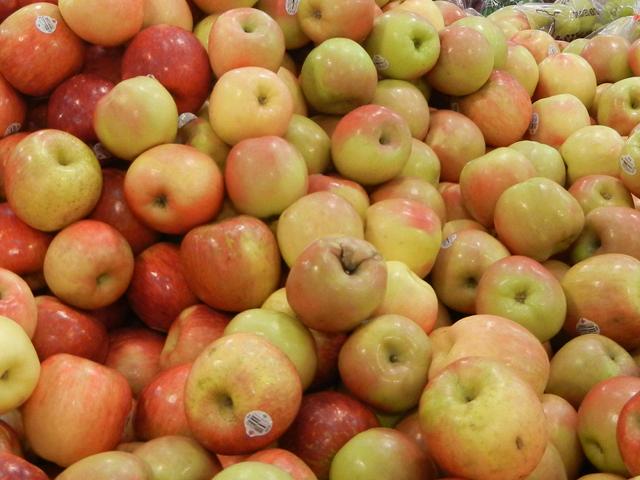 A bunch of Fuji apples, greenish and reddish, some with bruises