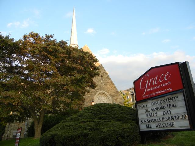 A church, with trees and bushes in front, and a church sign reading: Grace presbyterian church, the board saying holy discontent and having service times