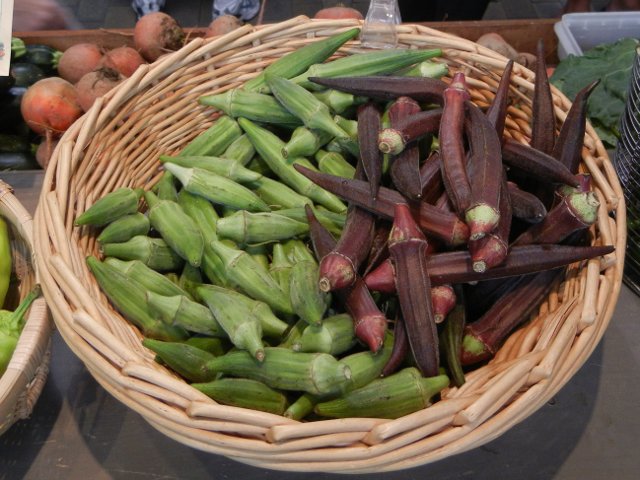 A basket containing fresh green okra pods on the left, and red okra pods on the right, with a few other vegetables around the edge of the photo