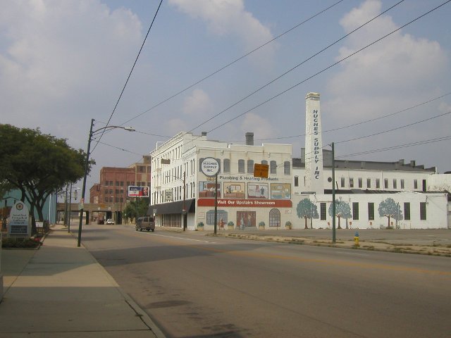A broad street in a mostly-empty industrial area, with a big white building reading Hughes Supply Inc