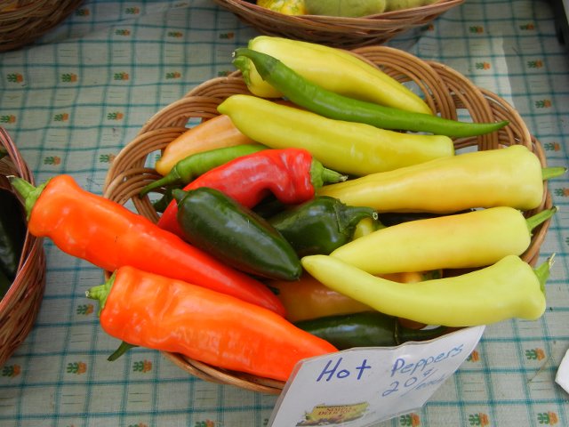 A basket of assorted hot peppers, orange, yellow, red, dark green and light green, and a sign reading: Hot peppers, 20 cents each
