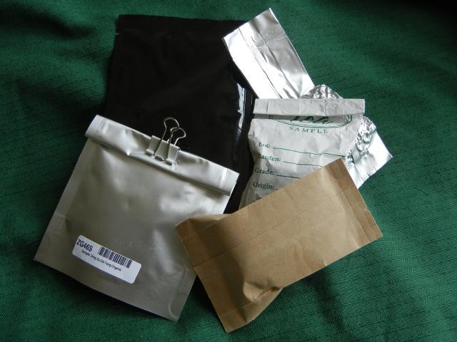 Various small container bags, paper, foil, shiny, silvery, black, brown, white, on a green background