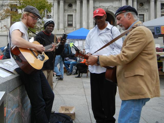 Three musicians, with two guitar players, and one man watching, at the Occupy Philly protest in front of city hall, Philadelphia