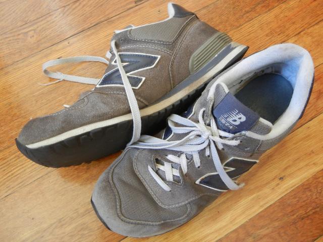 A relatively old pair of New Balance Classics 574 sneakers on a wooden floor