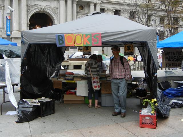 A gray tent with a colorful sign: BOOKS, with two people in it, and a bunch of books