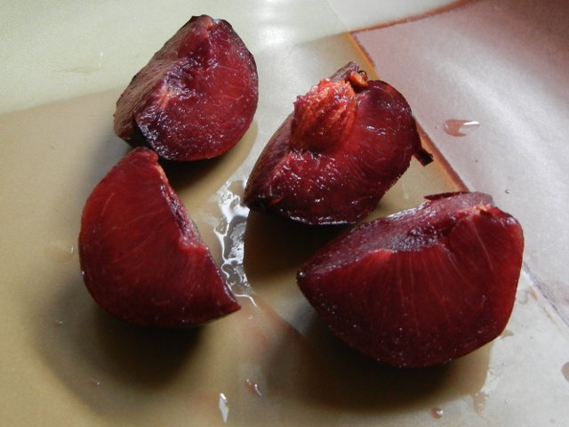 A sliced pomegranate pluot, a plum-like fruit showing dark purple flesh, on a brown ceramic plate