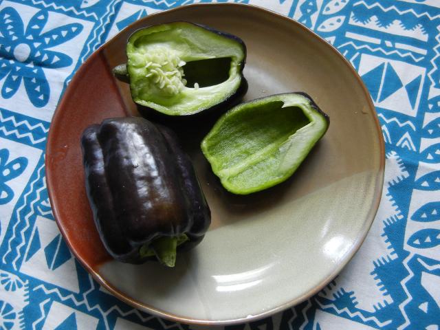 Two purple-black bell peppers, on a ceramic plate, one pepper sliced, showing bright green interior
