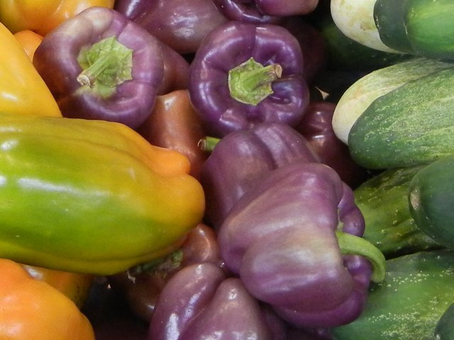 Purple bell peppers, a lighter purple with some paler areas, next to cucumbers and yellow-green bell peppers