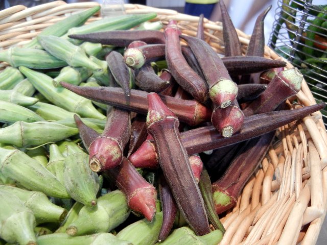 Red okra pods, in a basket, with green okra pods on the left