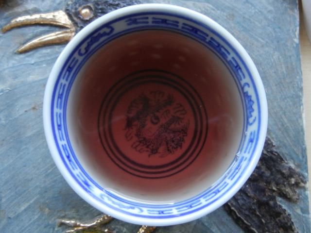 Small chinese teacup with brownish / reddish / purplish herbal infusion in it, on a hotplate