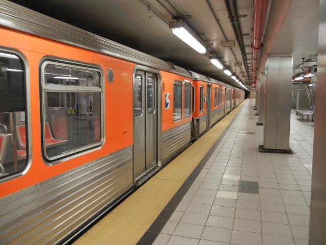 An orange subway train in a newish, mostly gray and silver subway station