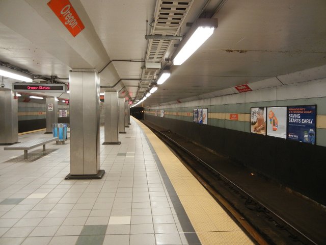 Interior of a subway station, clean, relatively new, with gray tile and orange signs reading: Oregon