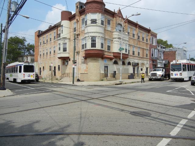 A city intersection with an attractive 3-story building with a turret, with a crossroads of trolley tracks in the street, and two trolleys right and left, one on each street