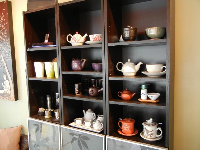A shelf with teapots, tea cups, and tea sets, in various styles and from various cultures