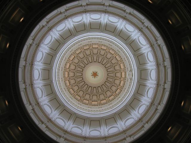 Looking up at a dome with round geometric patterns and a gold star with TEXAS inscribed around it.