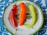 Three hungarian wax peppers on a colorful plate against a blue-and-white tablecloth, showing one bright red pepper, one bright orange, and one yellow-green
