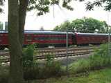 A historic train, painted red, reading: NORFOLK SOUTHERN, behind a chain-link fence on a bright, cloudy day