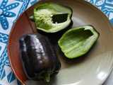 Two purple-black bell peppers, on a ceramic plate, one pepper sliced, showing bright green interior