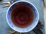 Small chinese teacup with brownish / reddish / purplish herbal infusion in it, on a hotplate