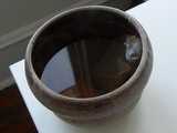 An unusual-shaped mug, handleless, with a tea bag and dark-colored tea in it