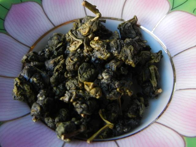 Loose leaf oolong tea, rolled in pellets, and with a greenish color, on a pink and green dish