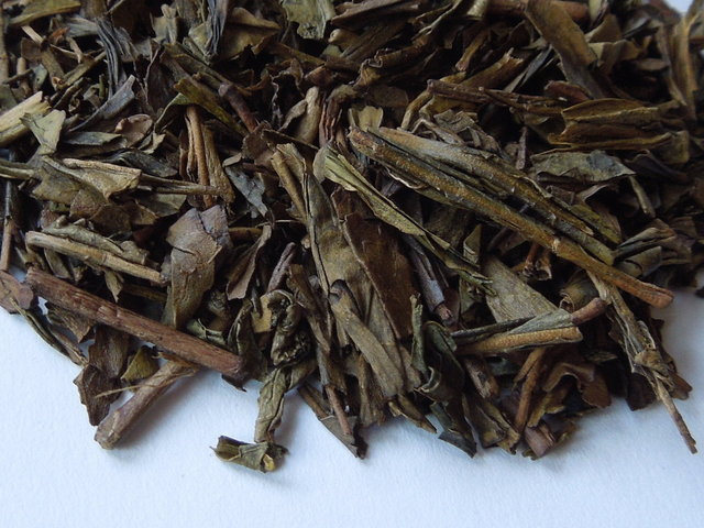 Closeup of roasted green tea leaves, showing dark brown, rolled appearance, with some twig