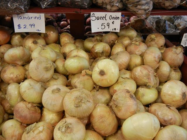Large, light yellow onions in a bin, with most onions having a visible flat shape, a sign reading: sweet onion, 59 cents -lb-