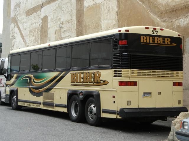 A coach bus parked in a parking lot in a city, with BIEBER written on the side