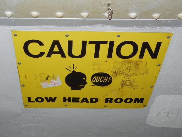 A sign on a low ceiling reading: caution, low head room, showing a picture of a person's head and a bump, with the person saying ouch