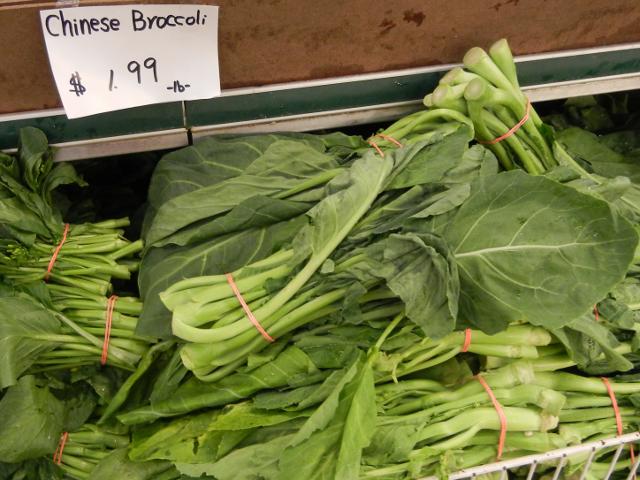 Raw chinese broccoli, a leafy green vegetable with long stalks, tied in bunches with rubber bands, with a sign