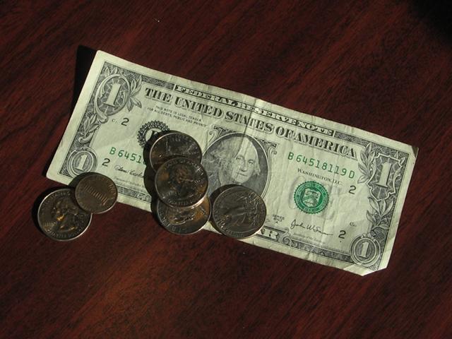 A dollar bill on a table, with four quarters on it, and one penny