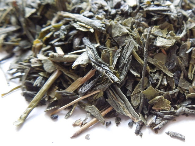 Closeup of green tea leaves, showing some twig and large, broken pieces