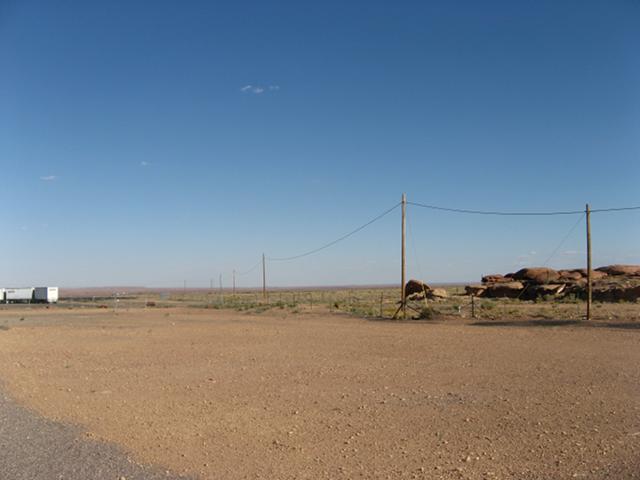 Barren gravel in the American west, a wire running on single posts, and some rocks
