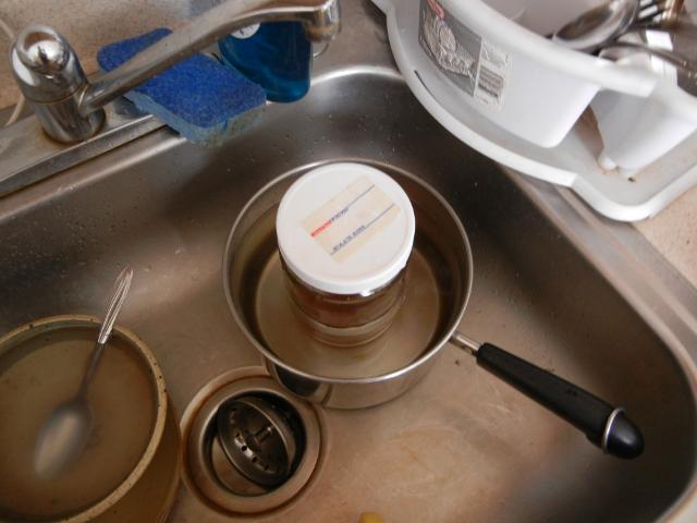 A pot in a kitchen sink, filled with water, with a closed jar sitting in it