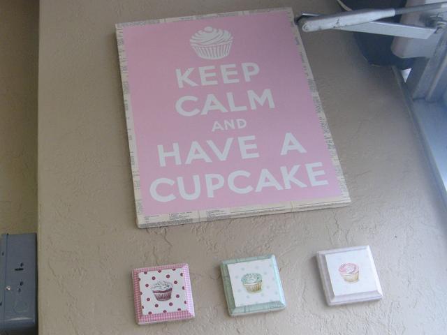 A pink sign with white lettering reading: Keep Calm and Have a Cupcake, with three little cupcake pictures beneath