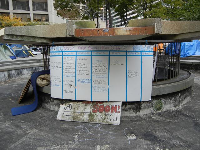 A large whiteboard in a dry fountain, reading: Occupy Philly education and Training Schedule
