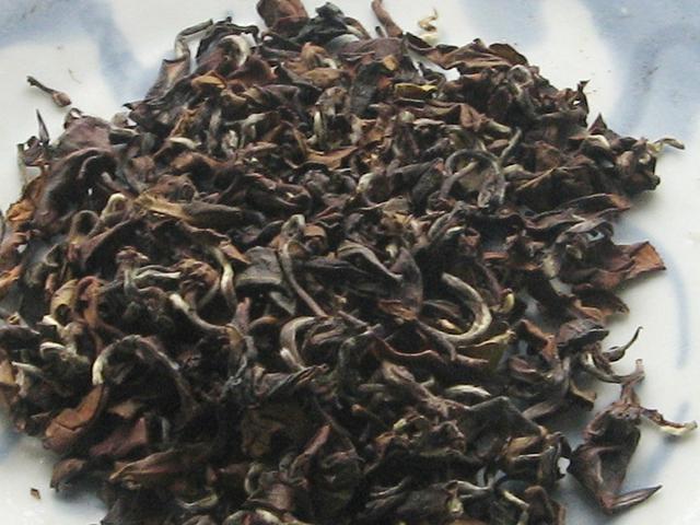 Leaves of oriental beauty oolong tea, showing dark brown, curved leaves, with some yellowish, reddish, black, and silvery accents