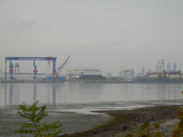 A river with the Philadelphia skyline on the right and some shipyard equipment on the left