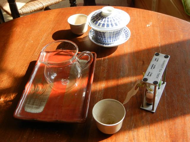 A lidded bowl with Chinese characters, hourglass tea timer, small glass jar on a plate, and two small teacups