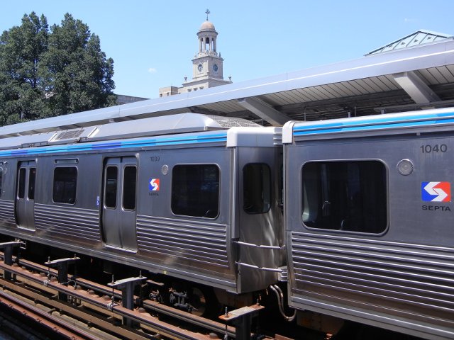 A SEPTA elevated train in a station, with a building's clocktower in the background