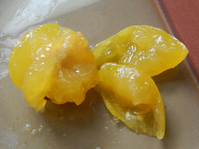 A yellow plum messily sliced open, on a ceramic plate, showing a messy juicy interior and juice all over the plate