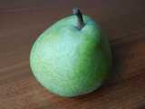 A green pear with an almost bluish tinge, on a wooden surface