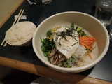 A bowl of bibimbap, assorted vegetables and egg, and rice on the side